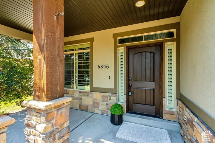 Covered front porch featuring stacked stone accents, a timber post, a wood-finish entry door, and transom windows