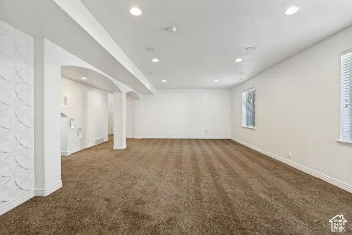 Open interior space featuring recessed ceiling lighting, three-dimensional geometric wall paneling, arched architectural detailing, and neutral wall-to-wall carpeting