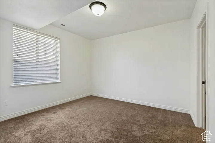 Neutral wall-to-wall carpeting, crisp white walls, window with horizontal blinds, and central flush-mount ceiling lighting
