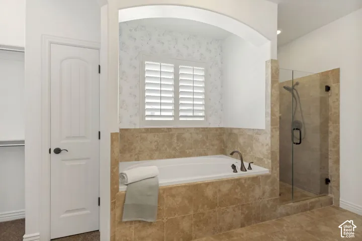 Built-in soaking tub with a tiled surround, arched alcove, plantation shutters, and a walk-in glass-enclosed shower