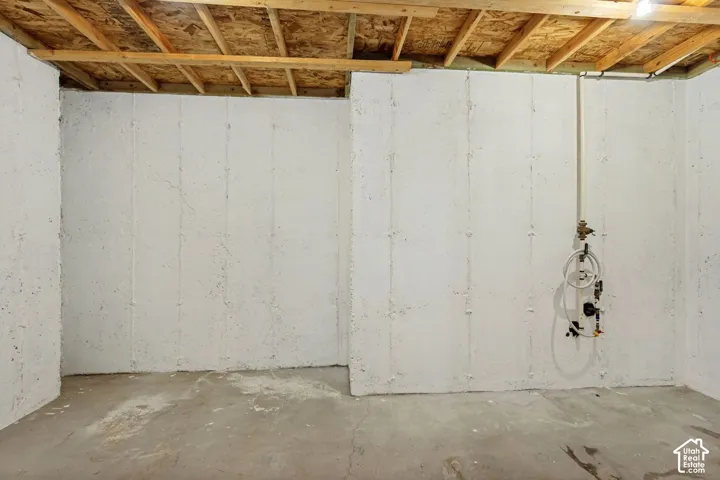 Unfinished space featuring white-painted concrete walls, exposed wood ceiling joists, concrete flooring, and exposed utility piping
