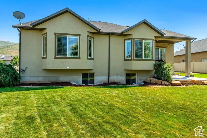 Stucco exterior featuring dual bay windows, a covered rear patio, rock-scaped garden beds, and an expansive lawn