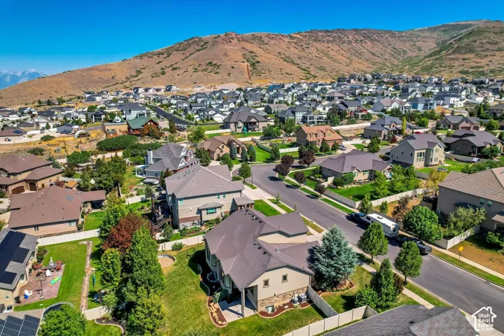Aerial perspective of a residential neighborhood featuring mountain topography, mature trees, manicured lawns, asphalt roadways, and suburban residences with composite shingle roofing