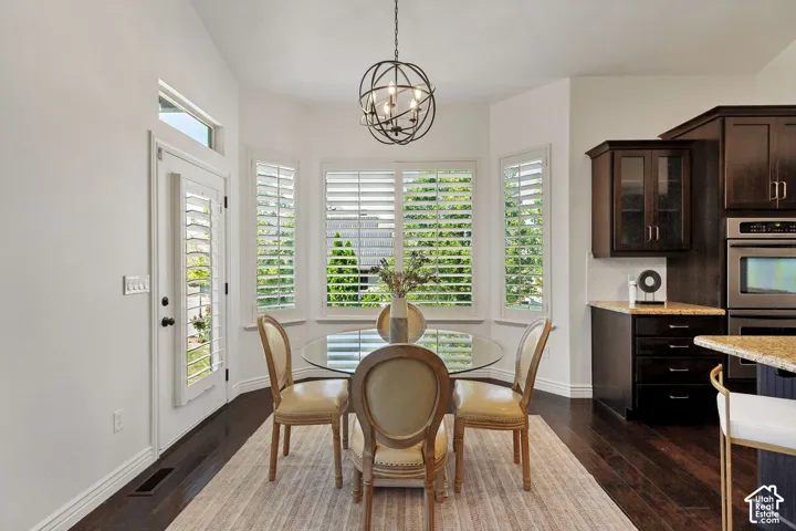 Vaulted ceilings, bay window with plantation shutters, orb-style pendant lighting, dark wood-finish flooring, and built-in wall oven
