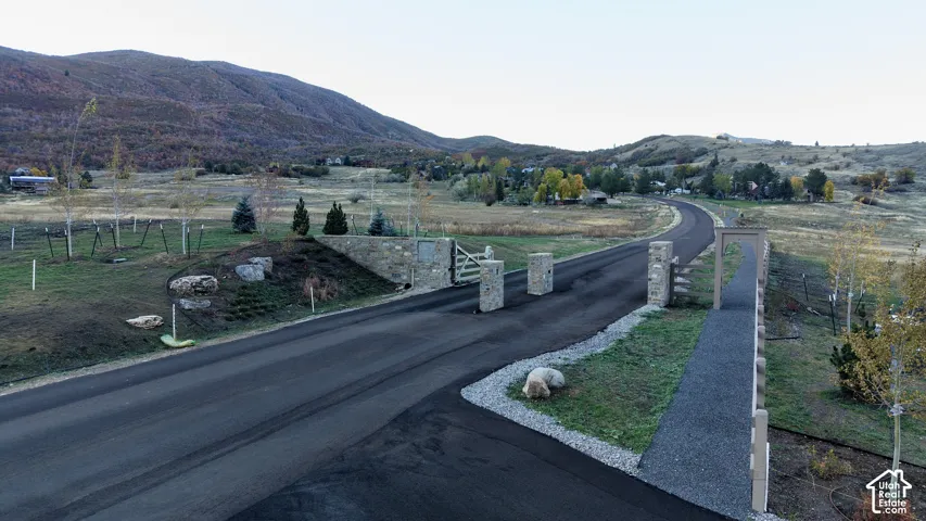 Gated entry featuring stone masonry pillars and metal fencing, paved asphalt driveway, stone retaining wall, and mountain backdrop