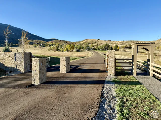 Gated stone entry featuring masonry pillars, paved driveway, timber-style fencing, and mountain backdrop