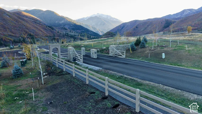 Paved access road featuring stone-column gated entry, three-rail fencing, and surrounding mountain scenery