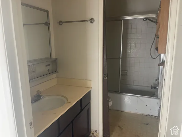 Bathroom featuring a vanity with an integrated basin, metal medicine cabinet, shower-tub combination with sliding glass doors, and tiled shower surround