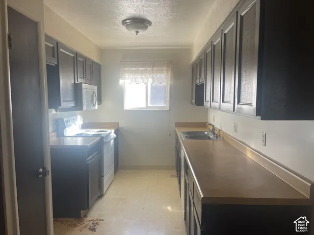 Galley-style kitchen featuring dark-toned cabinetry, laminate countertops, a double-basin stainless steel sink, and a built-in microwave