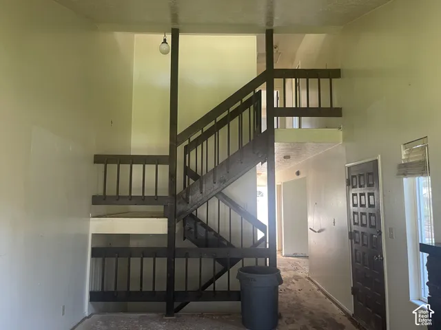 Multi-level interior space featuring an open staircase with dark-finished wood railings, a mezzanine-level balcony, and a multi-panel entrance door