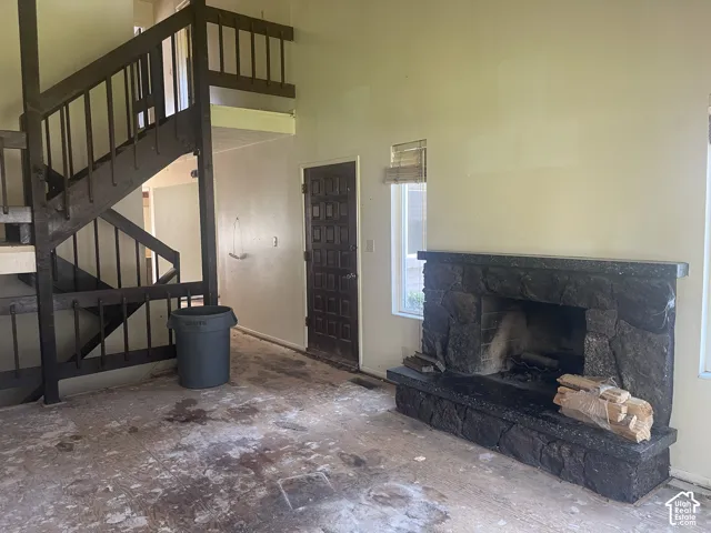 Vaulted ceiling space featuring a full-height stone fireplace with a raised hearth, an open wood staircase with railing, and a multi-panel entry door