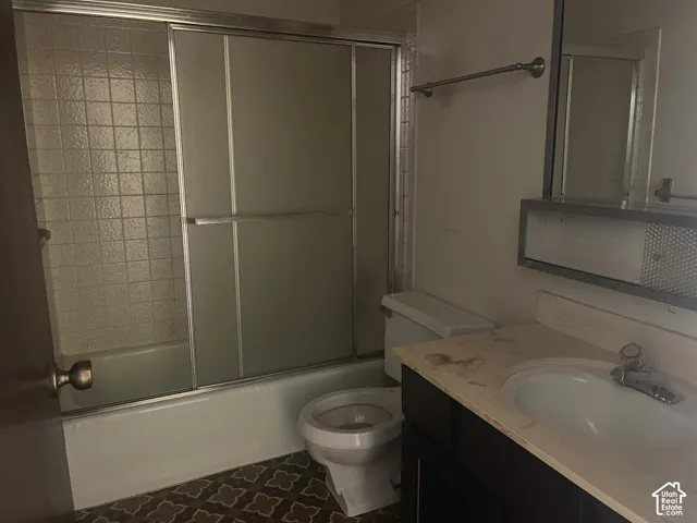 Bathroom featuring a vanity with a light-toned countertop, integrated basin, sliding-glass tub enclosure, tiled shower surround, and patterned flooring