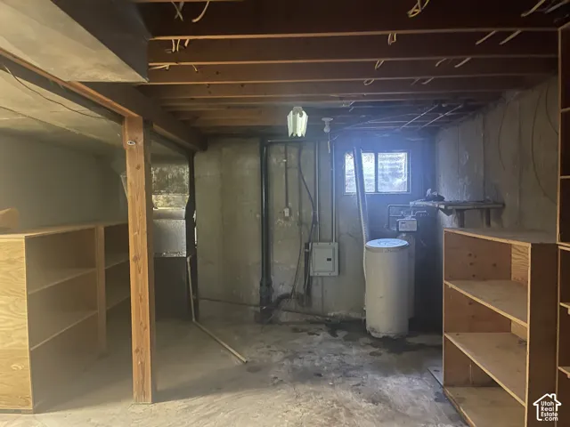 Unfinished storage space featuring exposed wooden ceiling joists, concrete foundation walls, built-in wooden shelving units, and a water heater