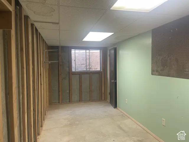 Room featuring exposed wood framing, concrete flooring, drop ceiling with recessed lighting, integrated pegboard wall paneling, and a horizontal sliding window