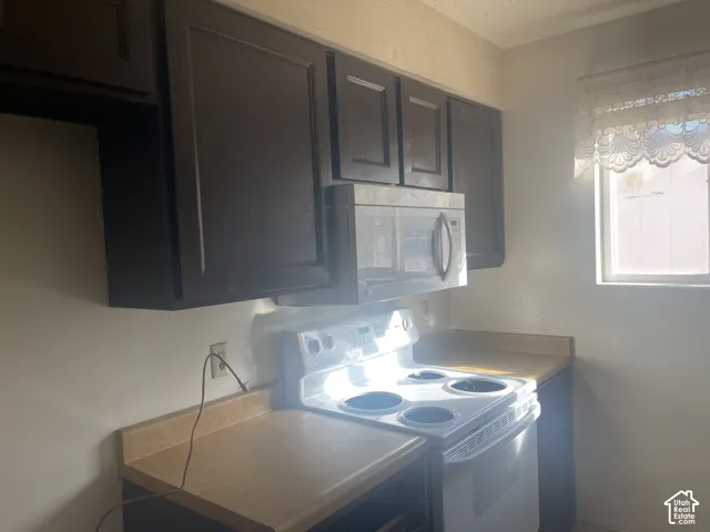 Kitchen featuring dark-finish cabinetry, solid-surface countertops, and a white freestanding electric range with an integrated over-the-range microwave
