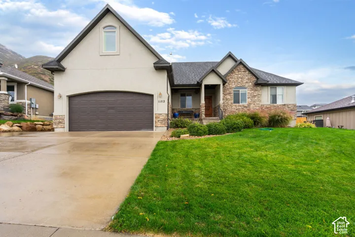 Exterior facade featuring a combination of stone veneer and stucco siding, a multi-gabled roofline, an attached two-car garage, and a manicured front lawn