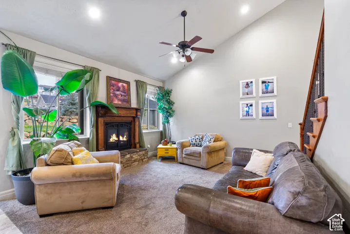 Vaulted ceiling featuring a central lighted ceiling fan, stone-surround fireplace with a wood mantel, recessed lighting, and a staircase with decorative metal balusters