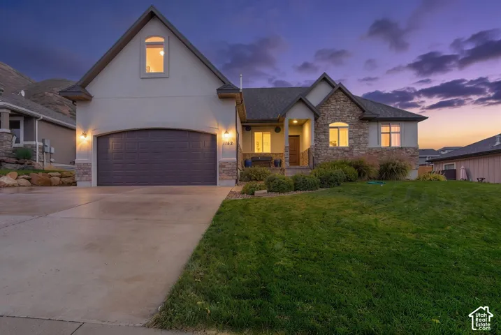 Multi-gabled exterior featuring stone veneer accents, stucco siding, arched garage entry, and concrete driveway