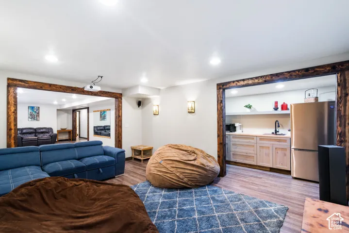 Open-concept space featuring rustic wood-beam door frames, wood-finish flooring, recessed lighting, and a kitchenette equipped with light-toned wood cabinetry and stainless steel refrigerator