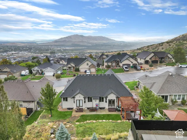 Aerial perspective of property featuring a concrete rear patio, wood-frame pergola, stone retaining walls, and mountain scenery