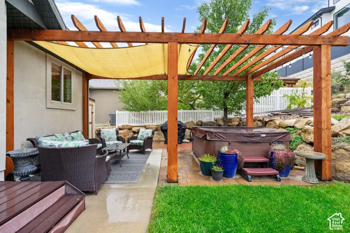 Outdoor patio space featuring a stained wood pergola with a retractable shade canopy, hardscaped pavers, and a built-in spa