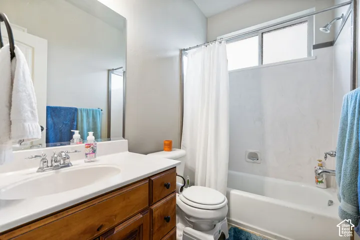 Bathroom featuring a wooden vanity, integrated basin with a chrome faucet, large wall-mounted mirror, and a tub-shower combination with a sliding window