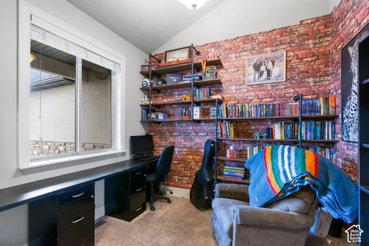 Vaulted ceiling, floor-to-ceiling brick-style accent wall, custom built-in industrial pipe shelving, and integrated black desk cabinetry