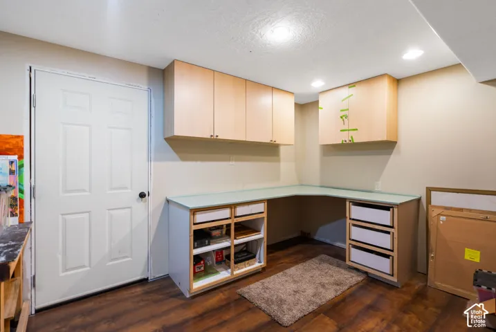 Built-in L-shaped desk with integrated drawer storage, overhead wood-finish cabinetry, recessed ceiling lighting, and wood-finish flooring