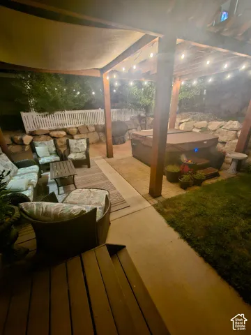 Covered patio featuring a timber-frame pergola, stone retaining wall, paver hardscaping, and built-in string lighting