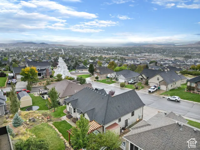 Elevated aerial perspective featuring a multi-pitched roofline, wood-slat pergola, landscaped terraced yard with boulder accents, and a wide-reaching panorama of distant mountains and surrounding valley