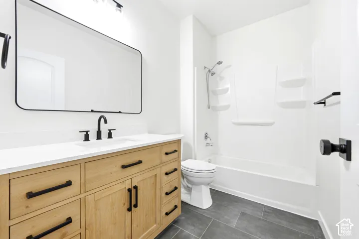 Light wood-finish vanity with white countertop, integrated rectangular sink, matte black hardware, large rectangular mirror, and gray tile flooring