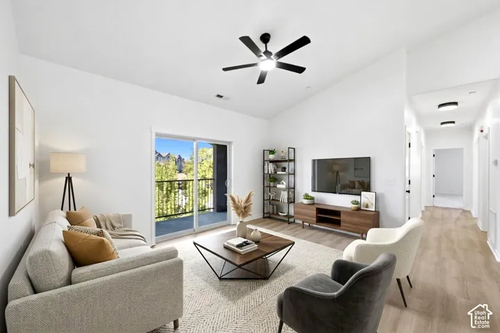 Vaulted ceilings, wood-finish flooring, sliding glass door leading to a balcony, and matte black ceiling fan with integrated lighting