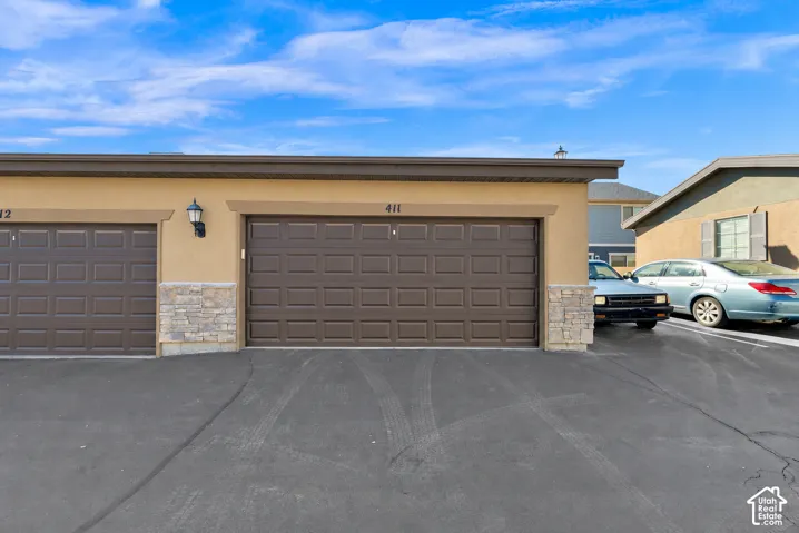 Single-car garage featuring a dark-finish sectional door, stucco exterior, stone-veneer accents, and wall-mounted exterior lighting