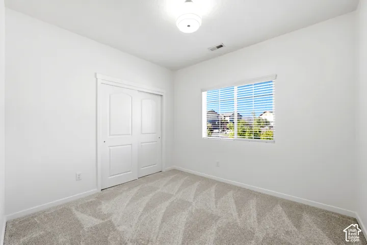 Interior room featuring textured carpeting, double-panel sliding closet doors, and a window with horizontal blinds