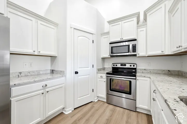 Kitchen featuring white shaker-style cabinetry, stone countertops, stainless steel appliances, and wood-finish flooring