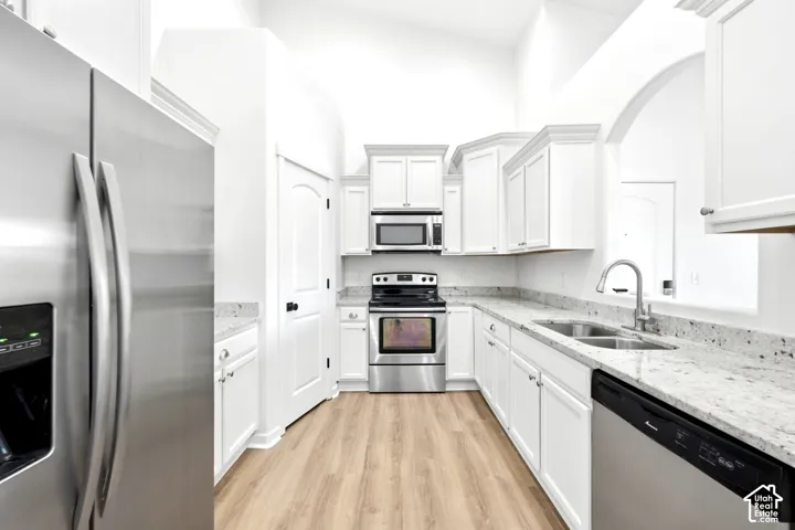 Kitchen featuring white cabinetry, light-toned stone countertops, stainless steel appliances, wood-finish flooring, and a high vaulted ceiling