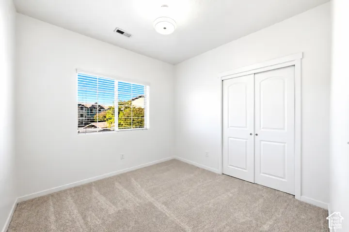 Neutral-toned wall-to-wall carpeting, dual-panel closet doors, single-window with horizontal blinds, and a semi-flush mount light fixture