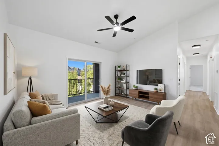 Vaulted ceilings, wood-finish flooring, matte black ceiling fan with integrated lighting, and sliding glass doors with exterior balcony access