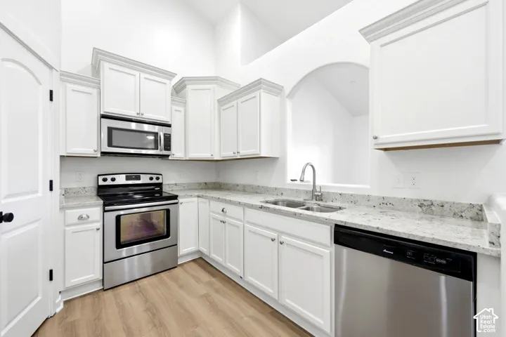 Kitchen featuring white cabinetry, stone-surface countertops, wood-finish flooring, and stainless steel appliances including a built-in microwave and range