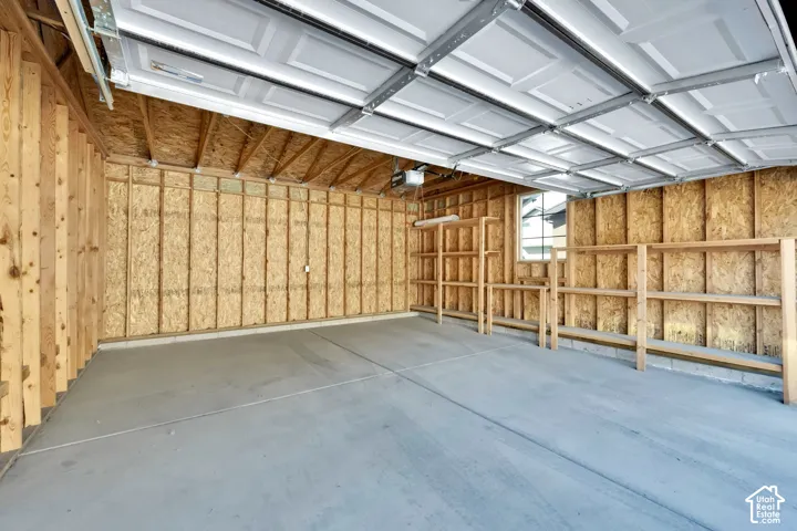 Garage interior featuring concrete flooring, exposed wood-frame walls, a multi-panel overhead door, and integrated wooden shelving