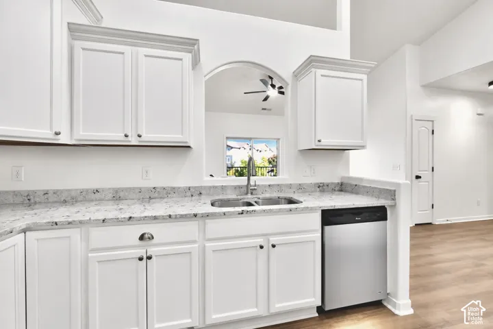 Kitchen featuring white shaker-style cabinetry, stone countertops, stainless steel dual-basin sink with arched faucet, stainless steel dishwasher, and wood-finish flooring