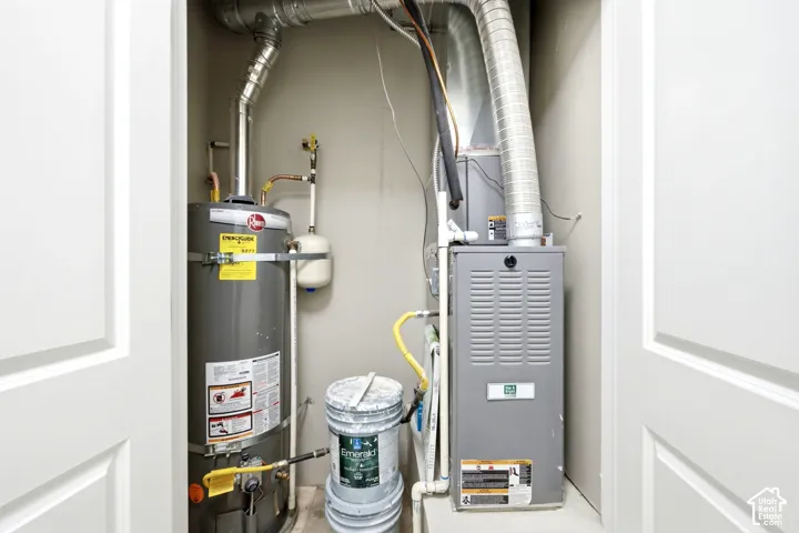 Utility closet housing a standard tank-style water heater and a high-efficiency forced-air furnace with rigid metal ducting and dual-door access