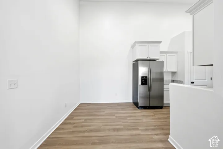 High-ceiling interior featuring wood-finish flooring, white shaker-style cabinetry, and a stainless steel side-by-side refrigerator