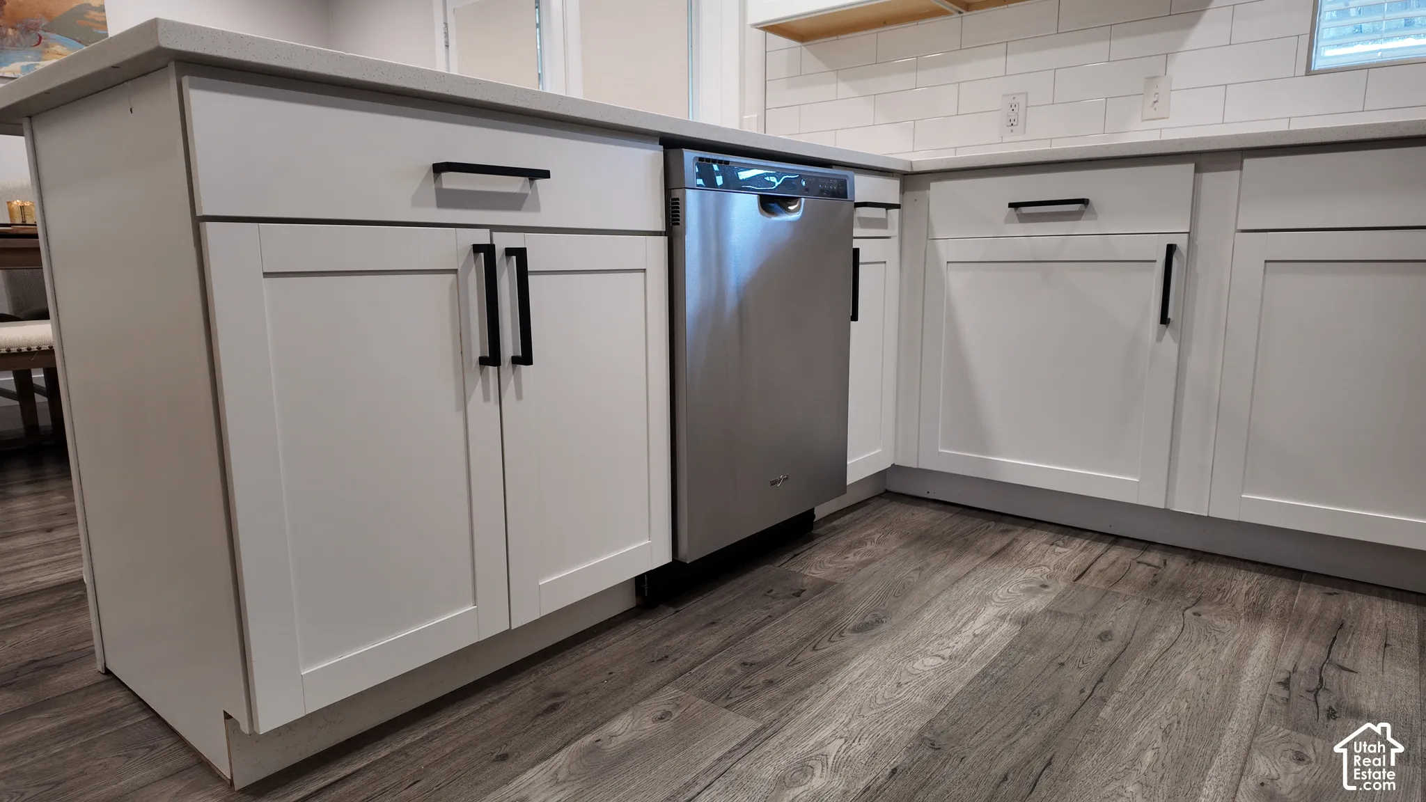 Kitchen island featuring white shaker-style cabinetry, matte black hardware, stone-finish countertops, stainless steel dishwasher, and subway tile backsplash over wood-finish flooring