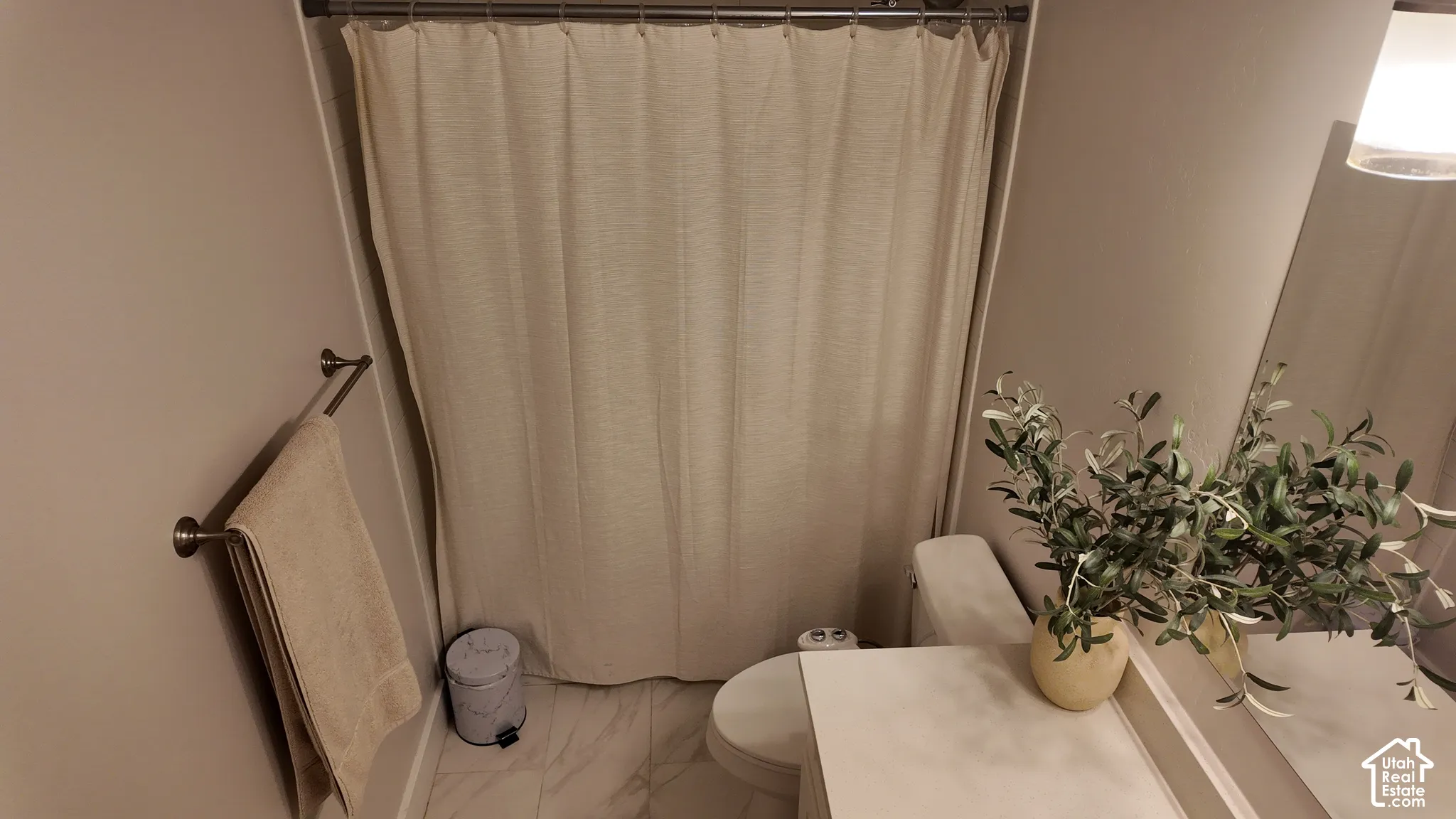 Bathroom featuring light-toned flooring with a subtle pattern, solid-surface vanity countertop, wall-mounted metal towel bar, and a full-height shower enclosure