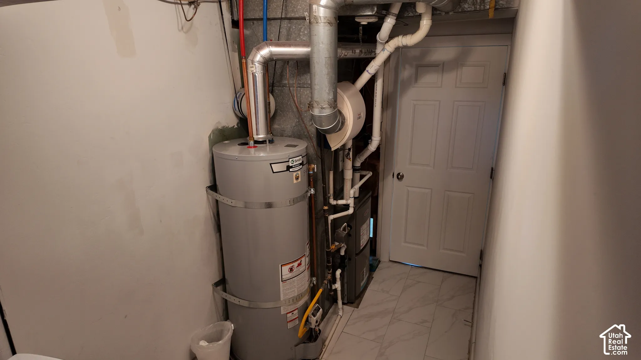 Mechanical utility space featuring a cylindrical water heater, forced-air furnace, exposed metal ductwork, and white tile flooring