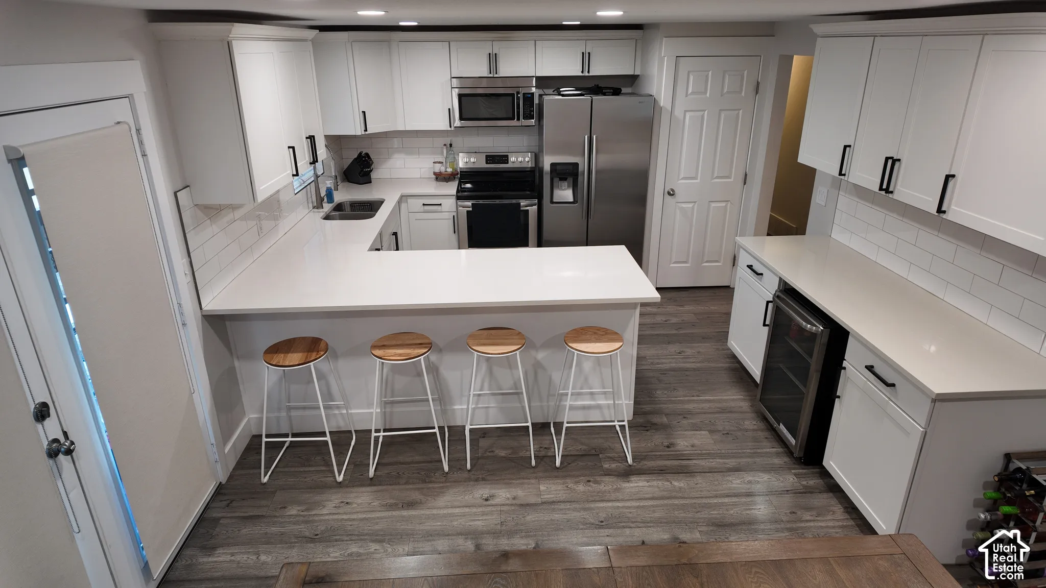 Kitchen featuring white shaker cabinetry, stone-finish countertops, subway tile backsplash, stainless steel appliances, and wood-finish flooring