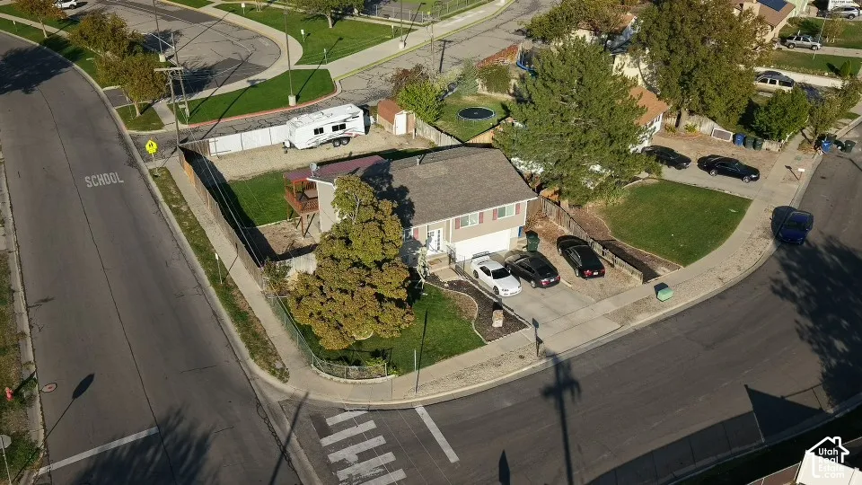 Corner lot residence featuring a two-car garage, concrete driveway, fenced yard, elevated wooden deck, and mature landscaping