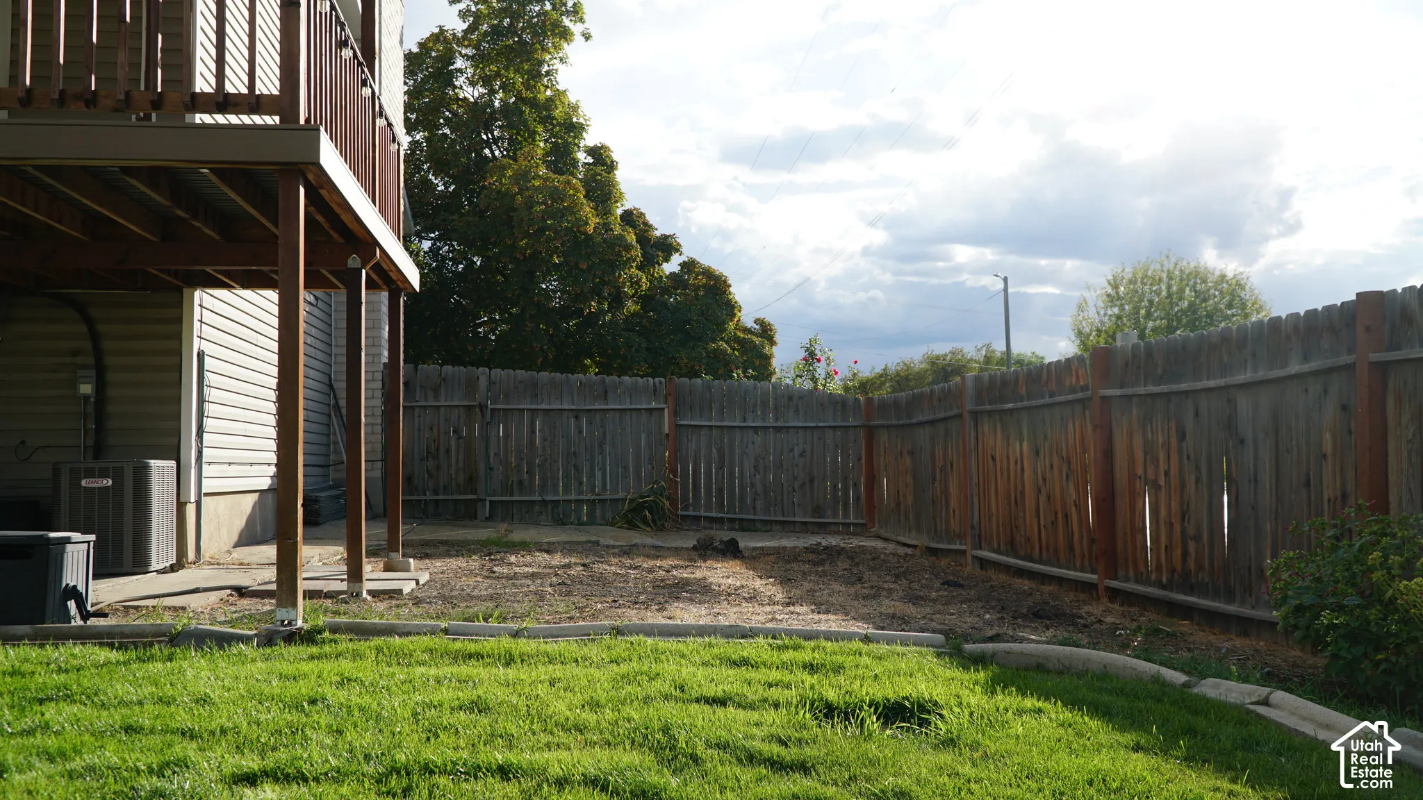 Backyard featuring a wood privacy fence, concrete patio, elevated deck, and a grass lawn with stone edging