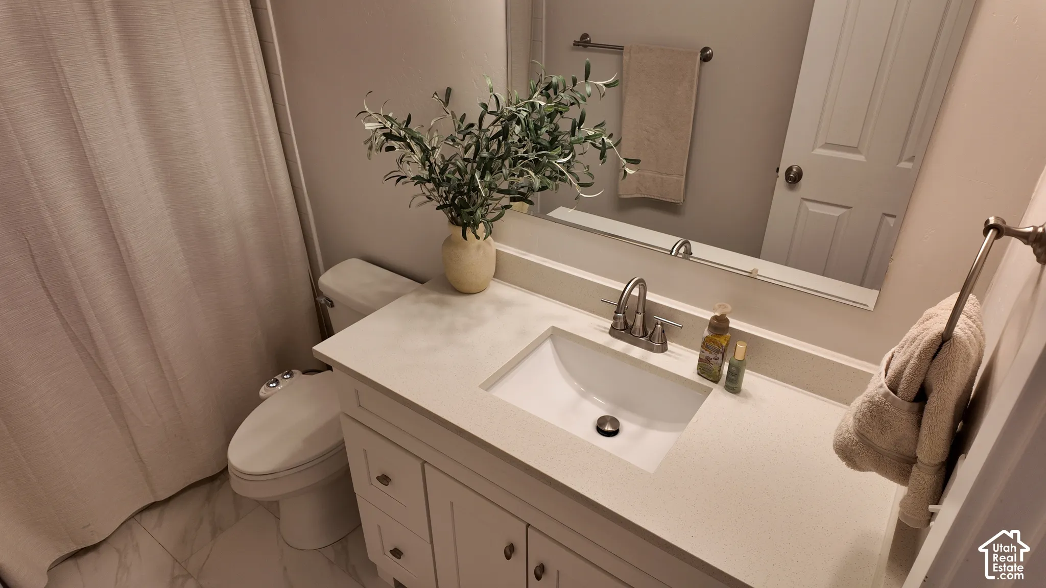 Bathroom featuring a vanity with a white composite countertop, an integrated rectangular sink, brushed nickel hardware, a full-width vanity mirror, and tile flooring